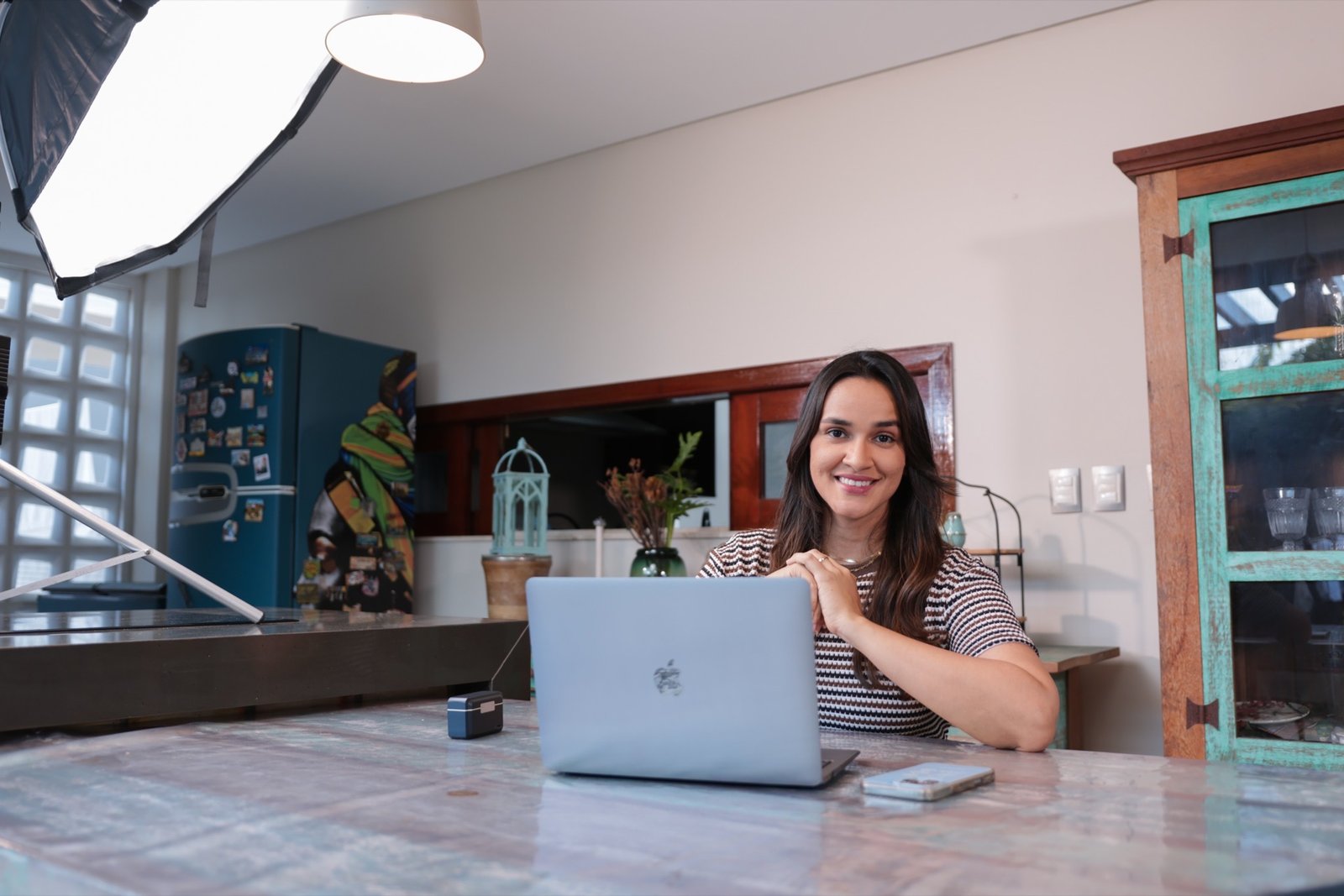 Izabel sentada à mesa com laptop, sorriso acolhedor — pronta para atendimento online